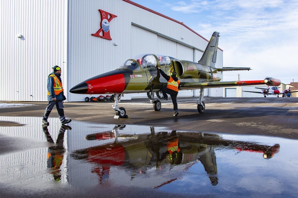 L39-5 grounds crew A red and green-coloured Aero Vodochody L-39C military aircraft parked with two grounds crew personnel inspecting the aircraft.