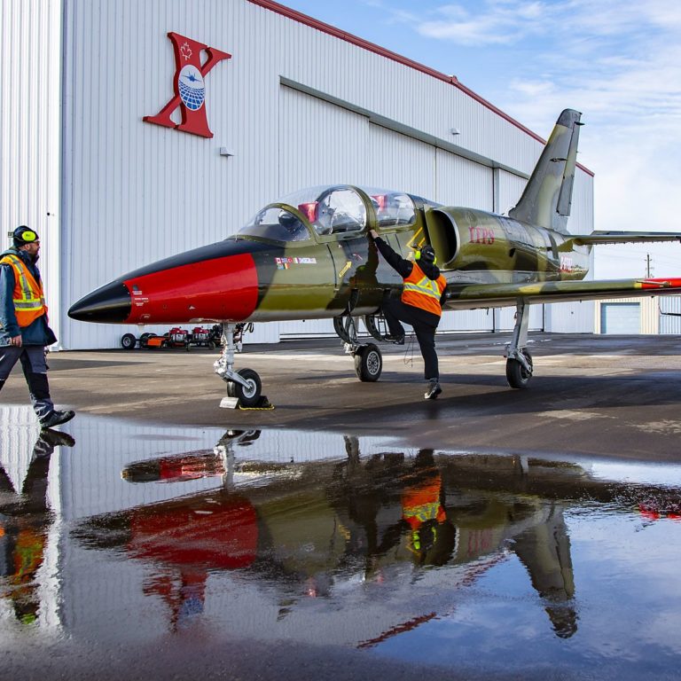 L39-5 grounds crew A red and green-coloured Aero Vodochody L-39C military aircraft parked with two grounds crew personnel inspecting the aircraft.