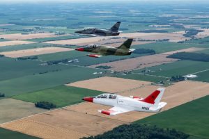 Photo of three jet airplanes flying over green and brown fields.
