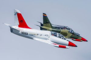 Photo of red and white and green L-39 jet aircraft flying in a blue sky.