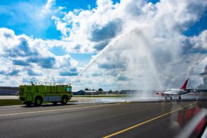 Photo of white and red jet aircraft being sprayed by water tanker.