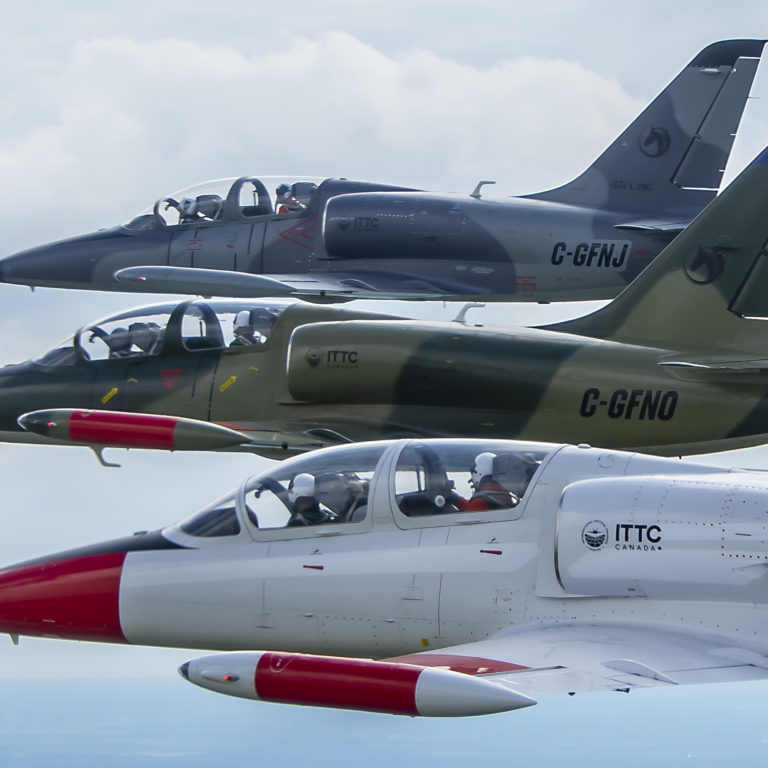 Photo of three L-39 Aircraft flying in formation with clouds and blue sky.