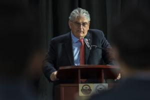 Photo of Giorgio Clementi in dark blue suit jacket speaking on a stage with podium.