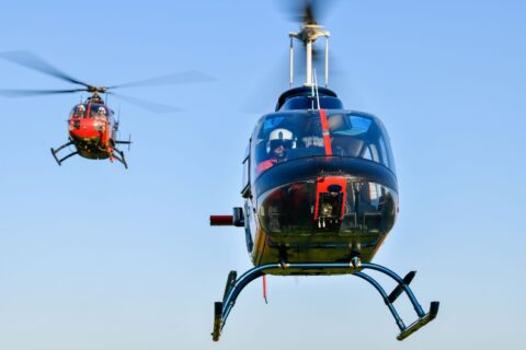 A black coloured helicopter in flight with a bright, red coloured helicopter in the background doing formation training..