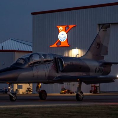 L-39-dusk-e1594927362932 Grey L-39 jet at dusk on tarmac beside building with a big red X.
