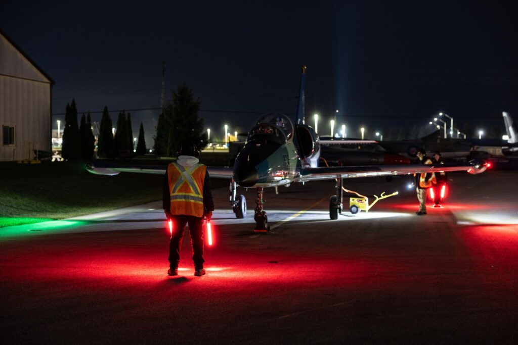 y (4) Flight line member stands in front of L39 on ramp during night flying operations